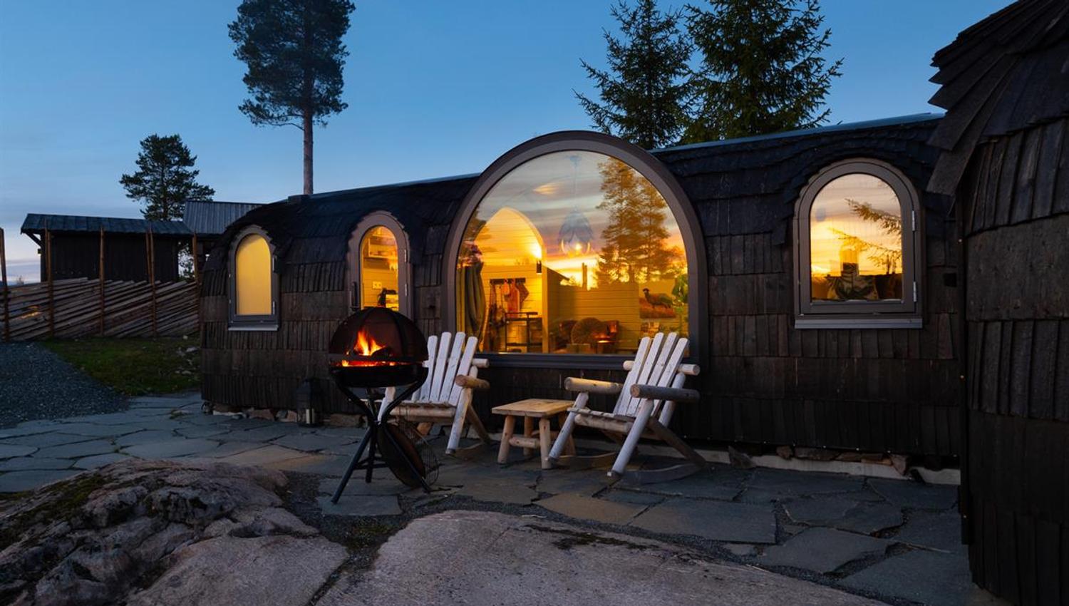 Oval wooden cabin pods with large windows and an outdoor seating area at dusk.