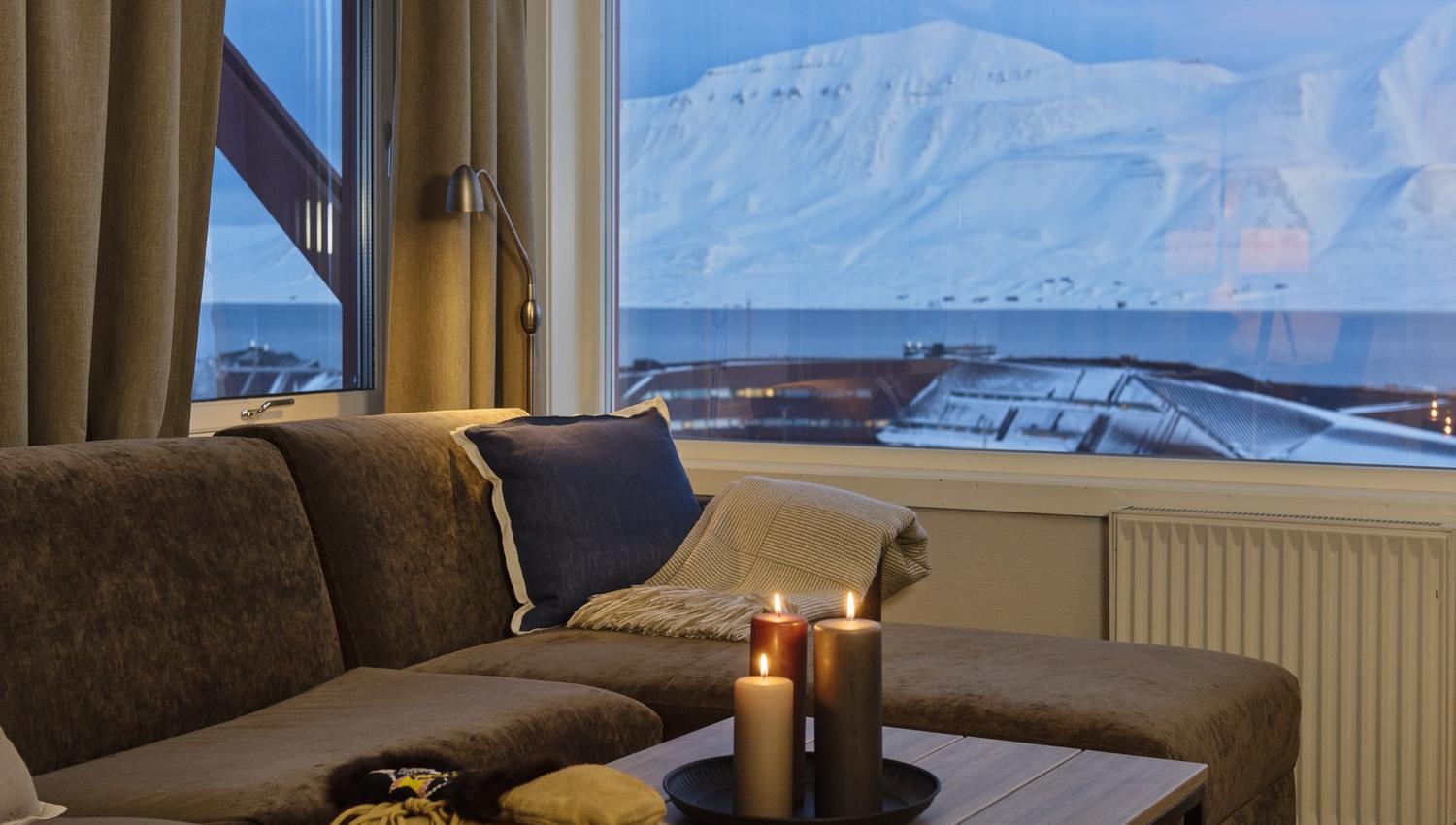 A couch with candlelights on a coffee table and a view towards snow-covered mountains in a blue light in the background