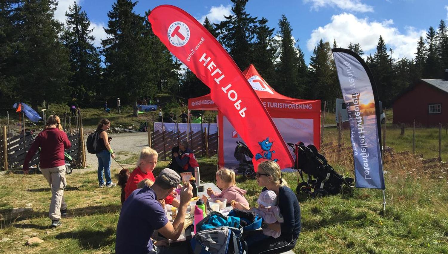 Kom deg ut‑dagen arrangert av HHT, der folk samles ute ved informasjonstelt og flagg i fint vær.