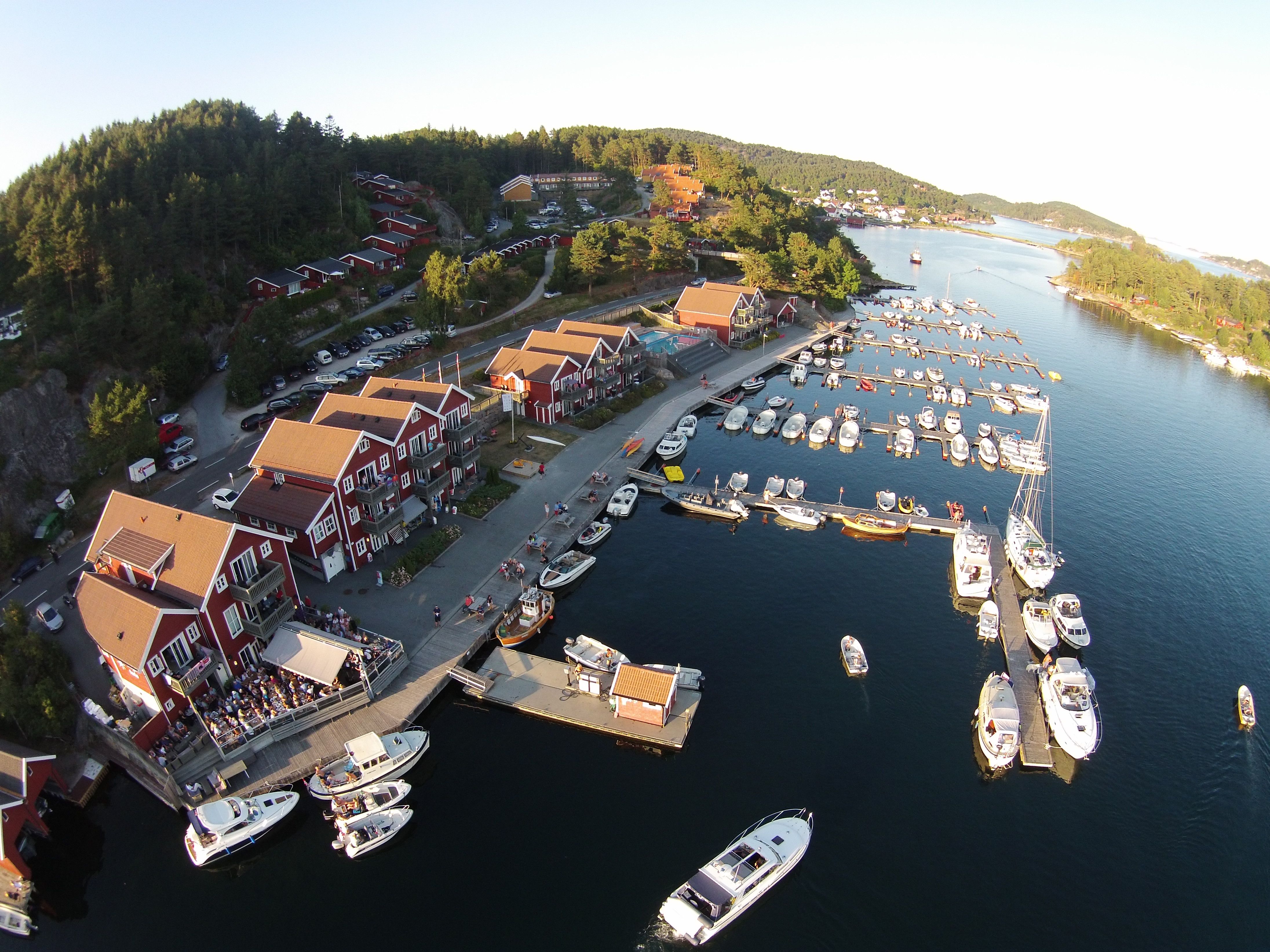 Aerial picture of a pier with many boats and several red buildings along the pier. At Tregde.
