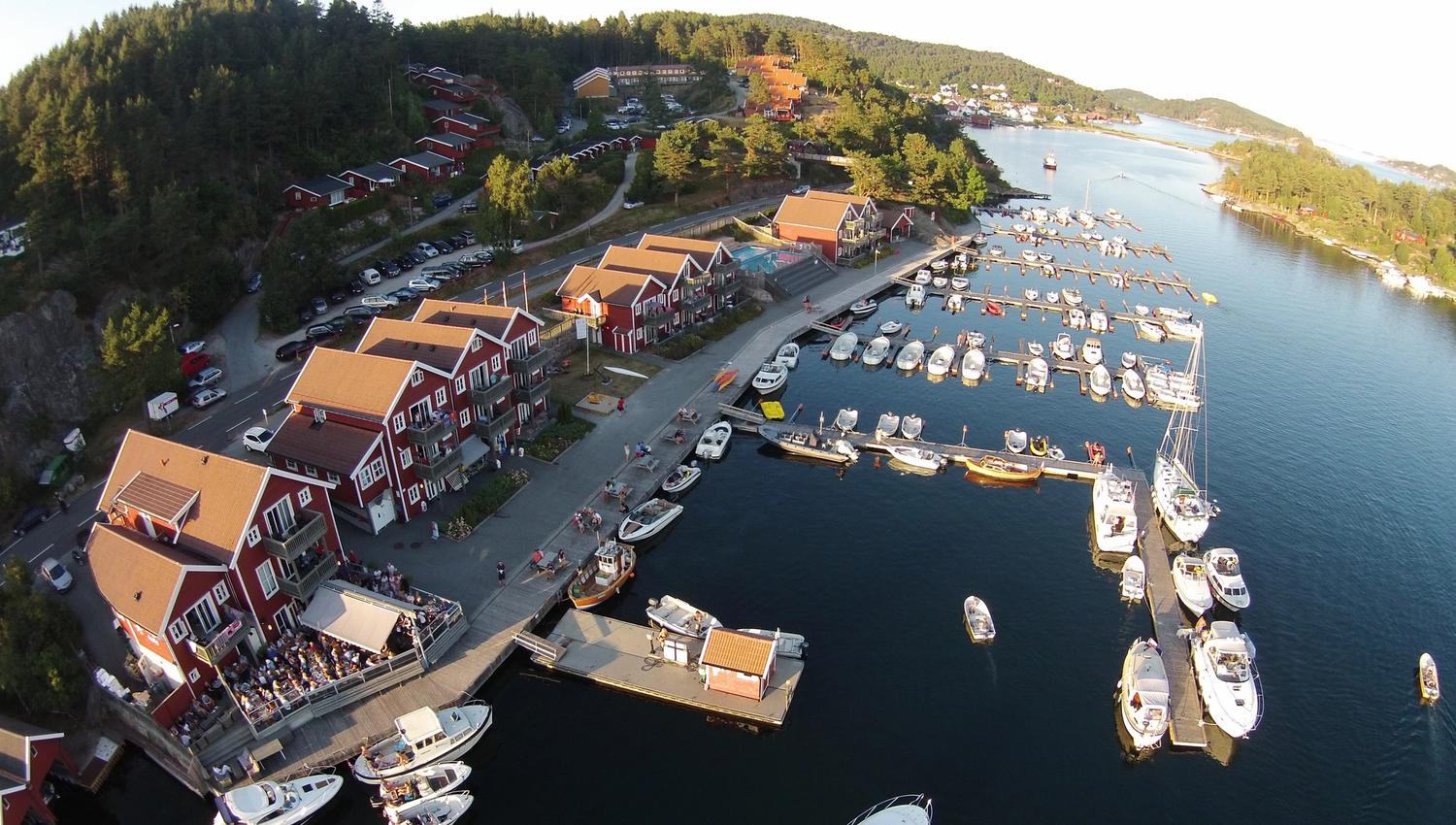 Aerial picture of a pier with many boats and several red buildings along the pier. At Tregde.