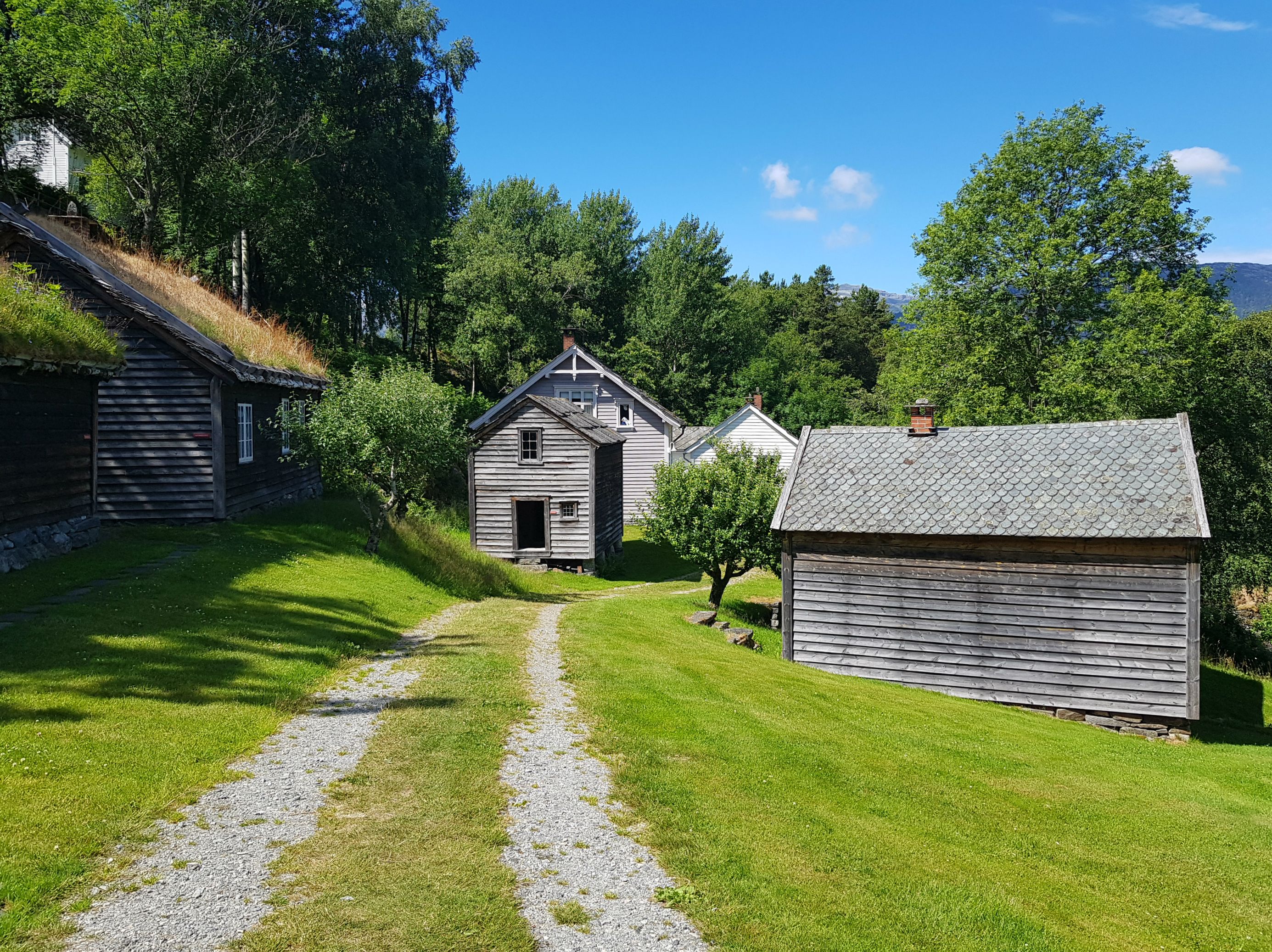 Gamle gardshus i grønt kulturlandskap i friluftsmuseet på Hardanger folkemuseum.