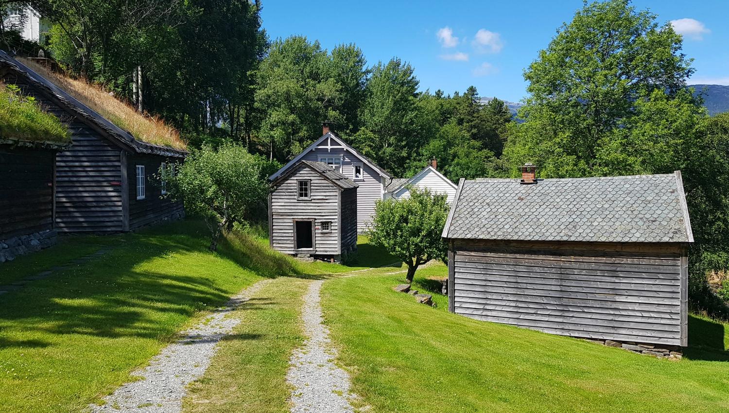 Gamle gardshus i grønt kulturlandskap i friluftsmuseet på Hardanger folkemuseum.