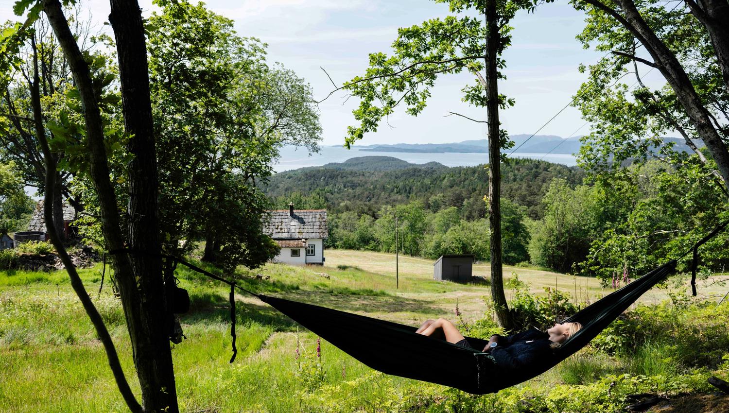 Person slappar av i hengekøye med utsikt over Hardangerfjorden ved Stigen Fjordlodge.