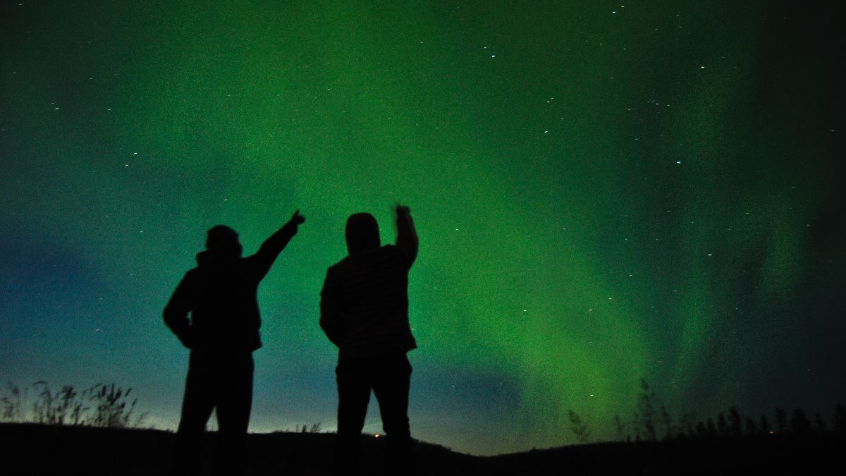 Two people pointing at the northern lights