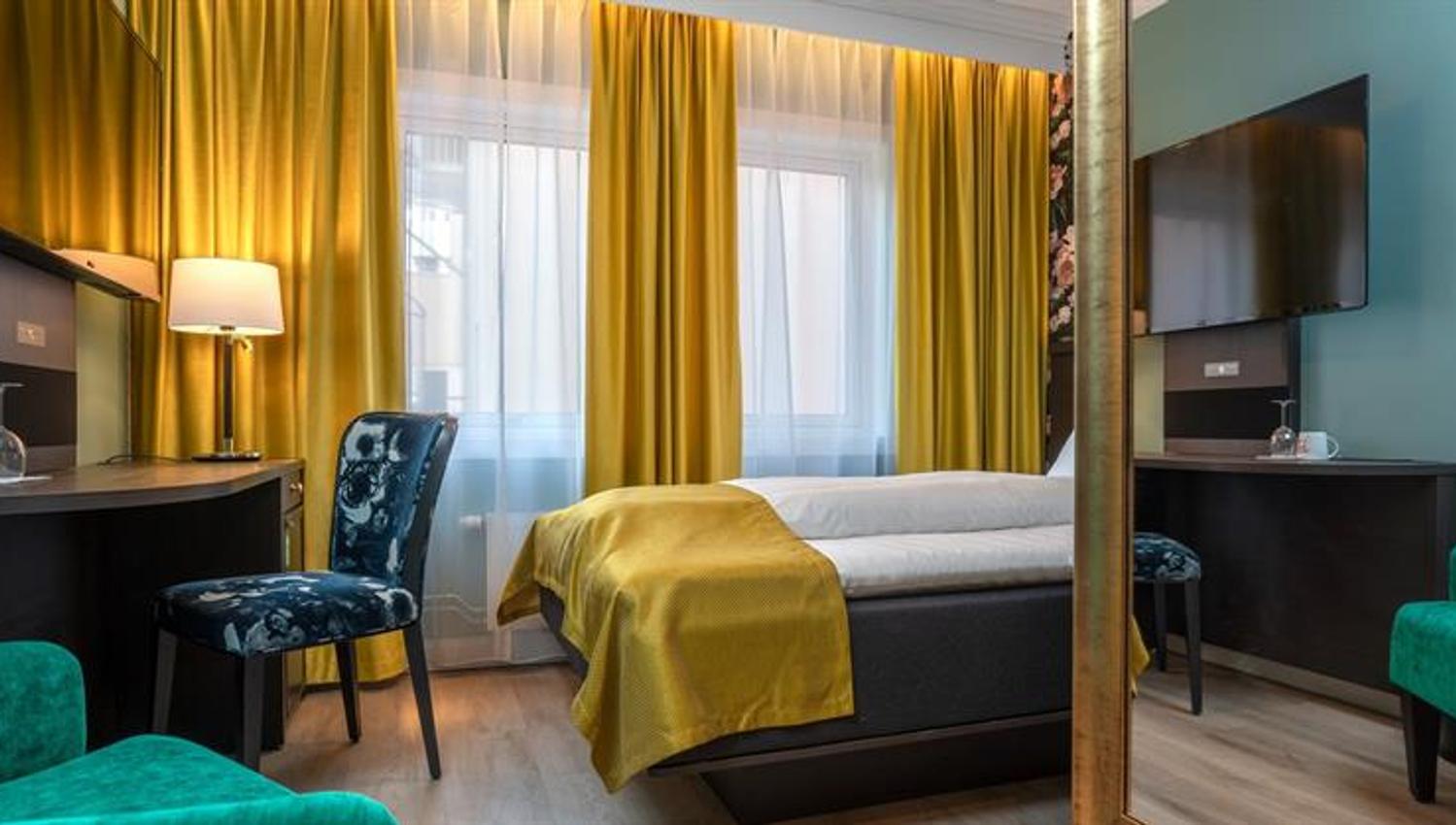 Soverom Thon Hotel Høyers. Gule gardiner, grønn stol, skrivebord, seng med gult teppe.