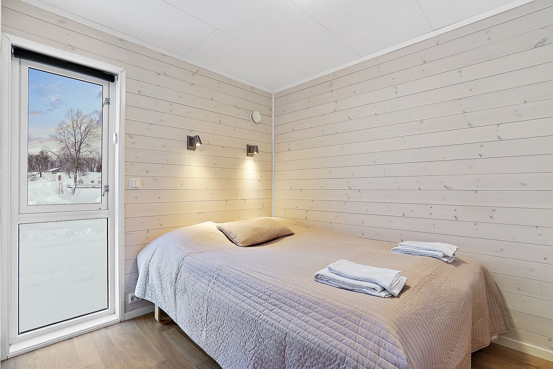 Bedroom with double bed, wooden walls, and view of snowy landscape