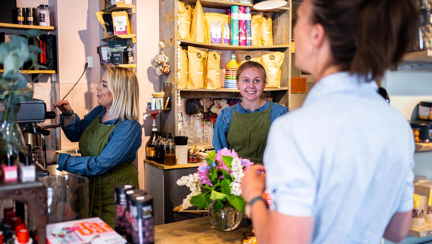 to damer som jobber i en butikk, som snakker med en kunde