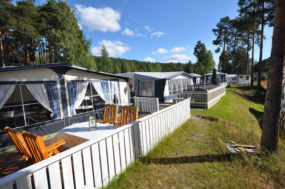 Permanent caravans with wooden deck and outdoor furniture, white fence and green lawn.