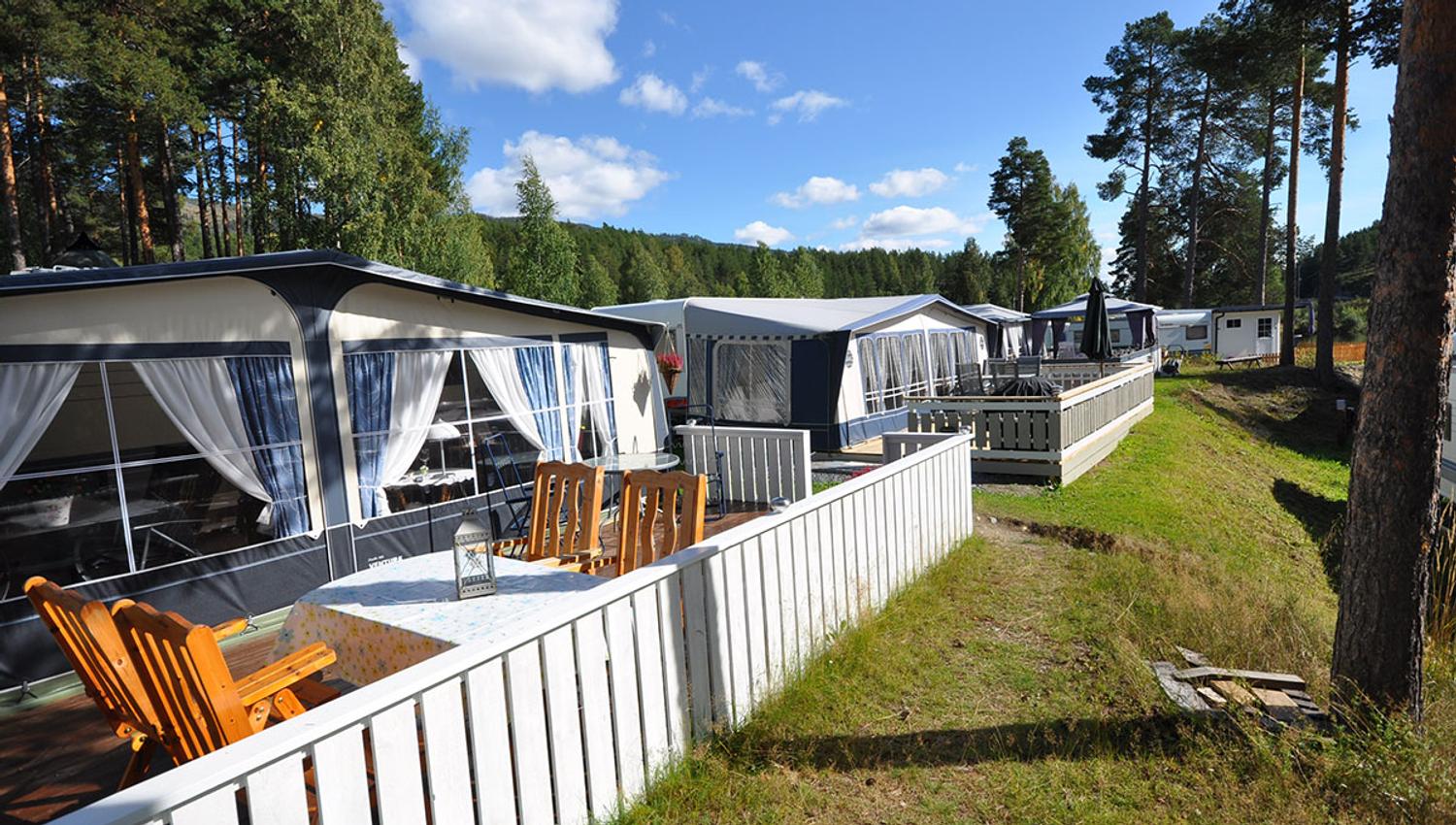 Permanent caravans with wooden deck and outdoor furniture, white fence and green lawn.