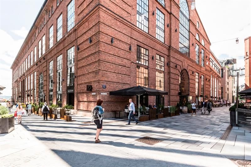 Sidegate med mennesker som går, brun mursteinsbygning, restauranter med uteservering.