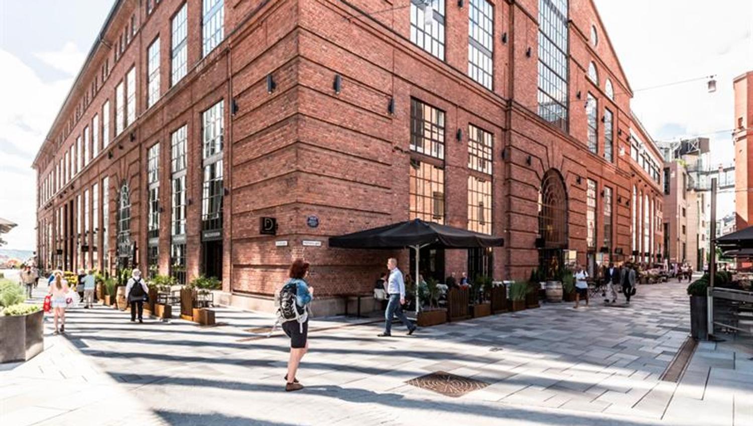 Sidegate med mennesker som går, brun mursteinsbygning, restauranter med uteservering.