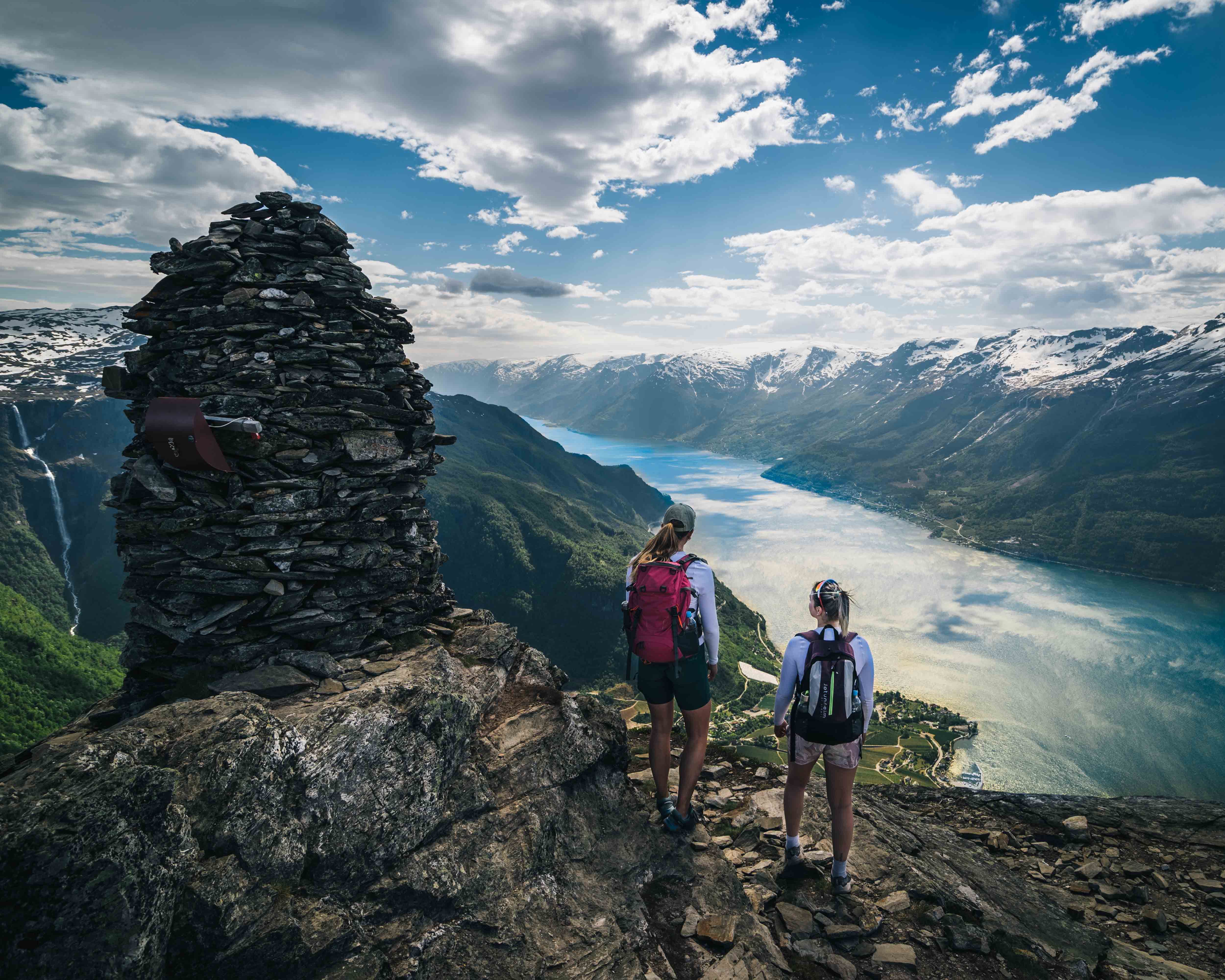 Hikers standing next to a cairn on Dronningstien with a spectacular view of the fjord.