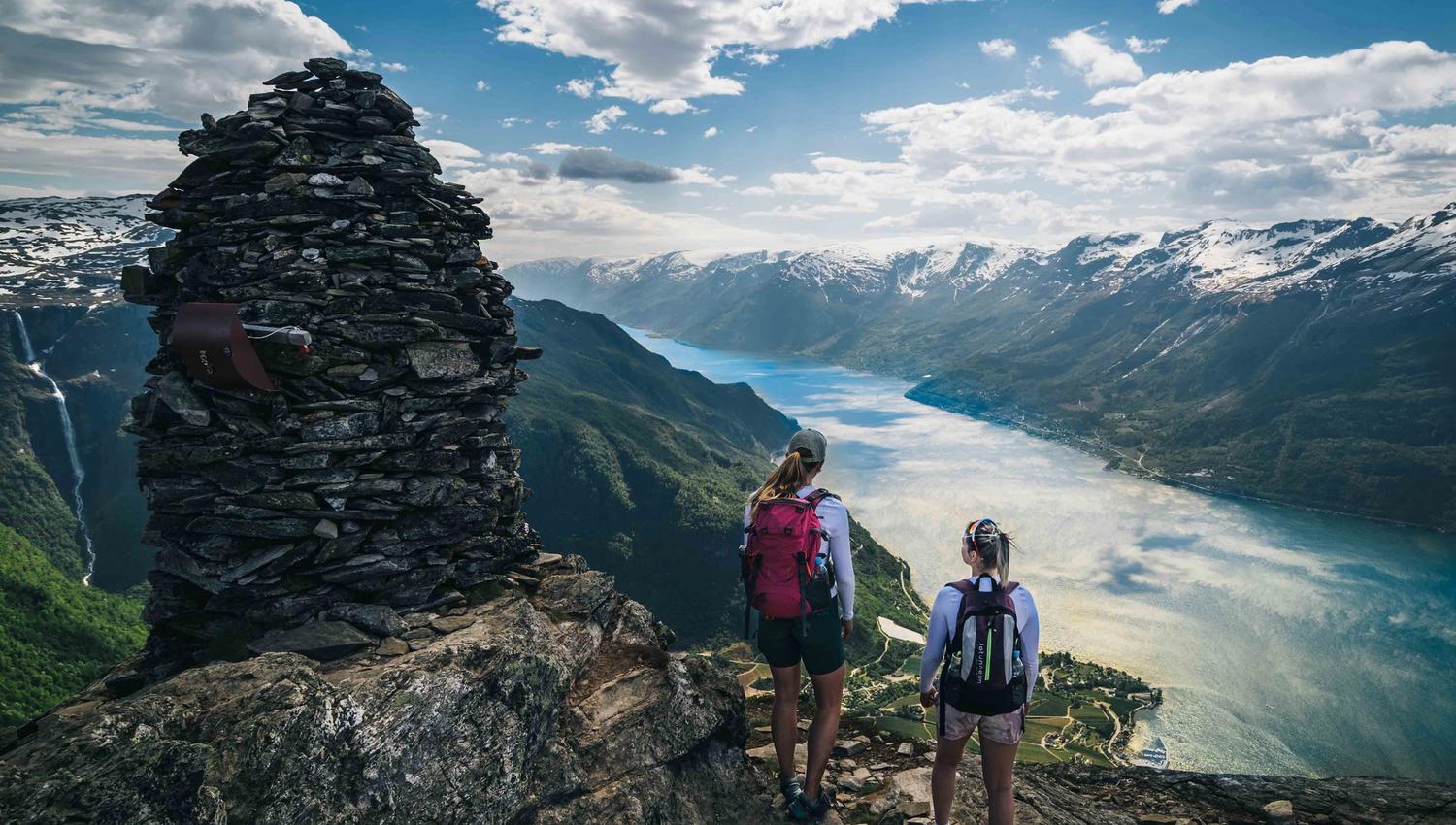 Hikers standing next to a cairn on Dronningstien with a spectacular view of the fjord.