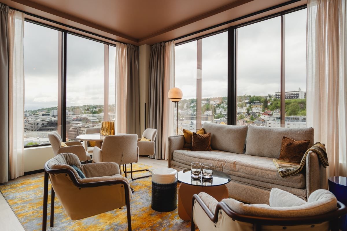 Living room with large windows, beige sofa, and view of city and greenery