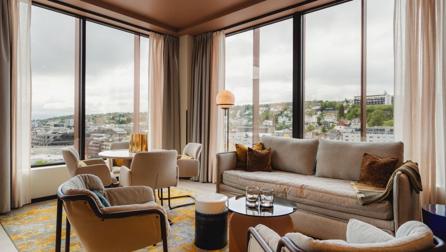 Living room with large windows, beige sofa, and view of city and greenery