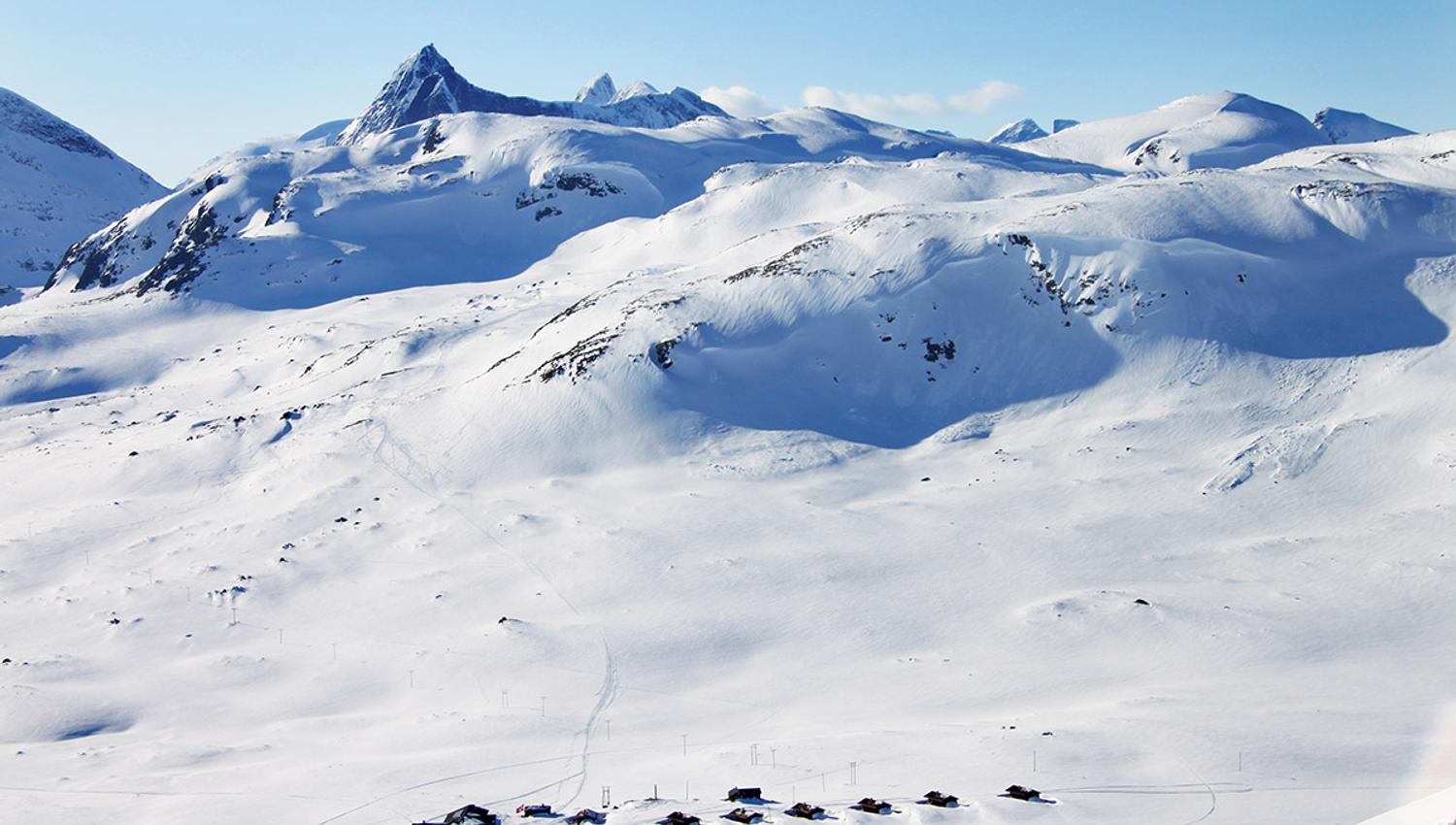 En liten fjellstue og et knippe hytter i et nedsnødd høyfjellslandskap fra fugleperspektivet