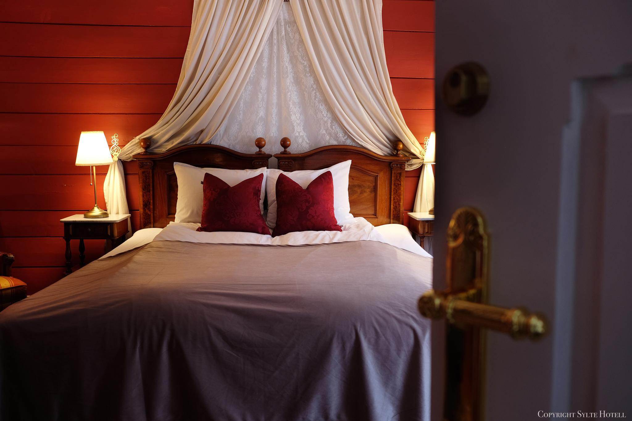 Et romantisk rødt rom med lyse gardiner over sengen.