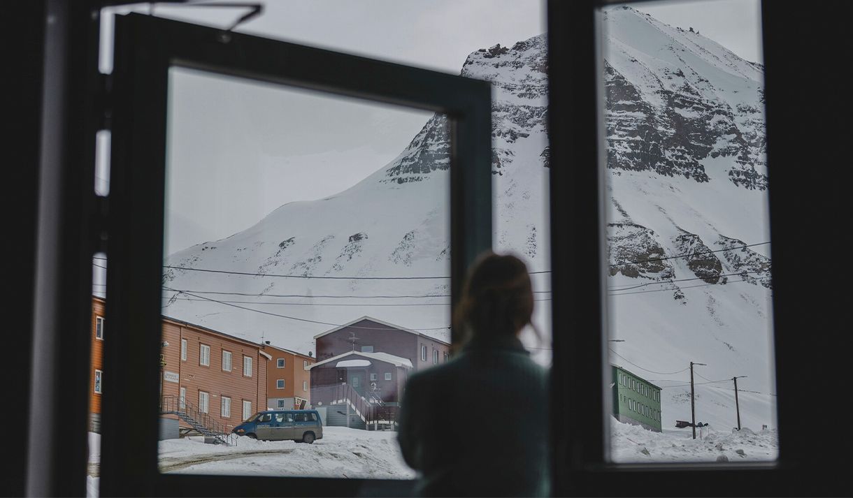 A guest in silhouette in the foreground looking up at a mountain and colourful buildings in snowy surroundings in the background