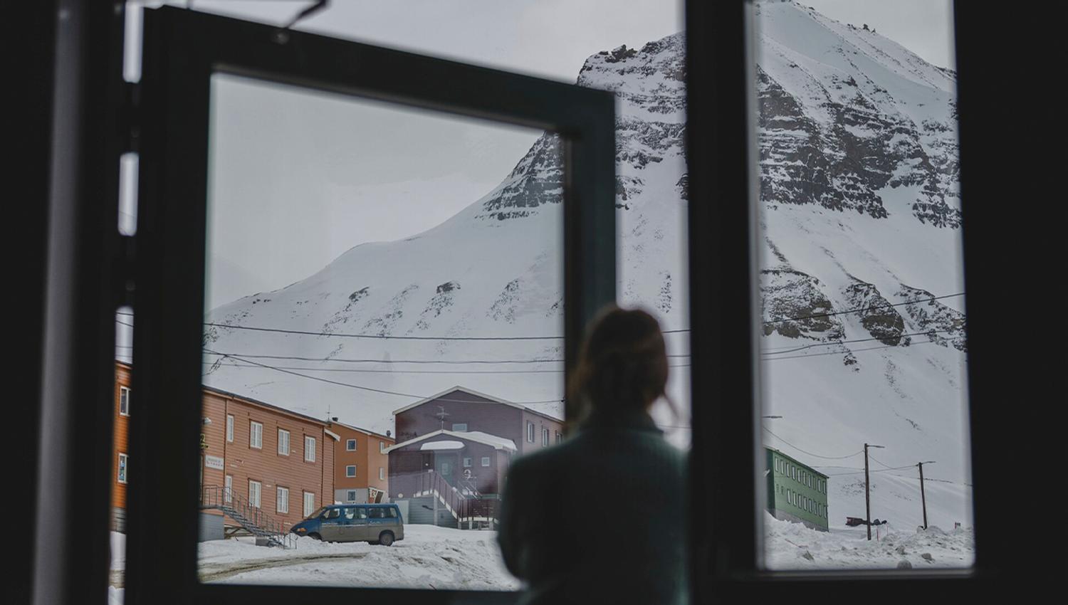 A guest in silhouette in the foreground looking up at a mountain and colourful buildings in snowy surroundings in the background