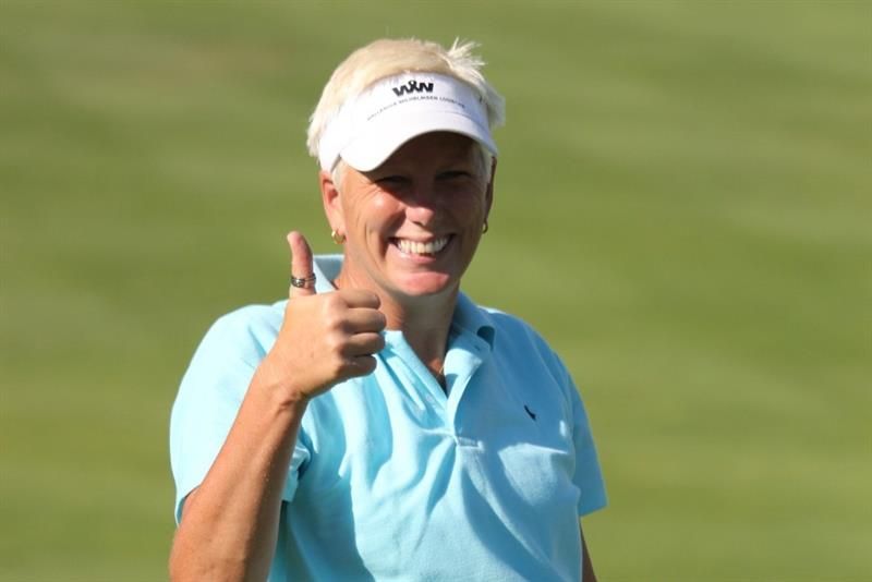 en dame som smiler mot kamera hun står på en golfbane