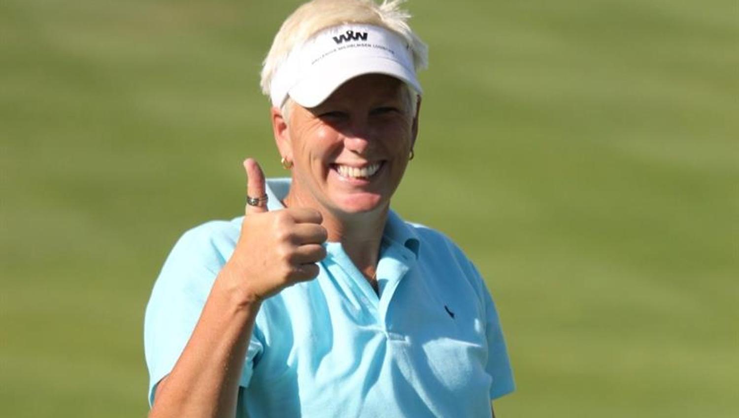 en dame som smiler mot kamera hun står på en golfbane