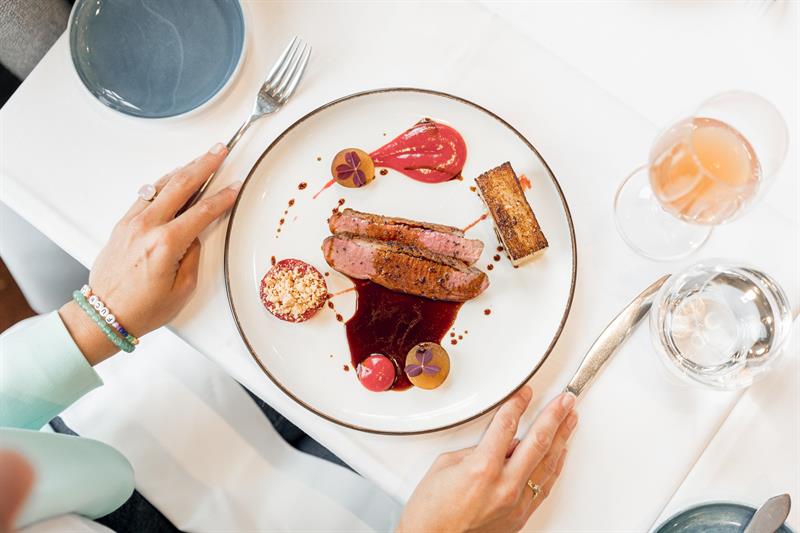 Beautifully plated main course with meat, green peas and sauce served on a white tablecloth.