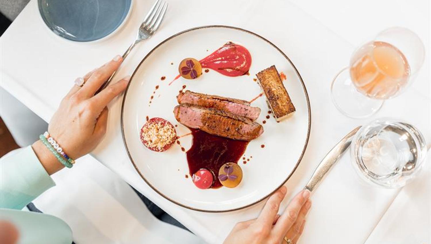 Beautifully plated main course with meat, green peas and sauce served on a white tablecloth.