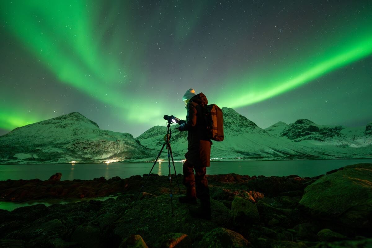 En fotograf peker sitt kamera mot nordlyset som buer seg ovenpå