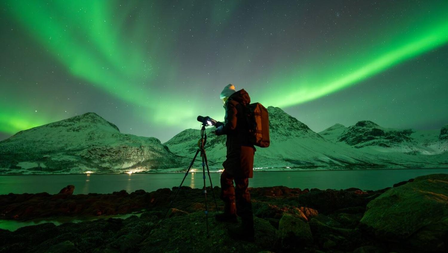 En fotograf peker sitt kamera mot nordlyset som buer seg ovenpå