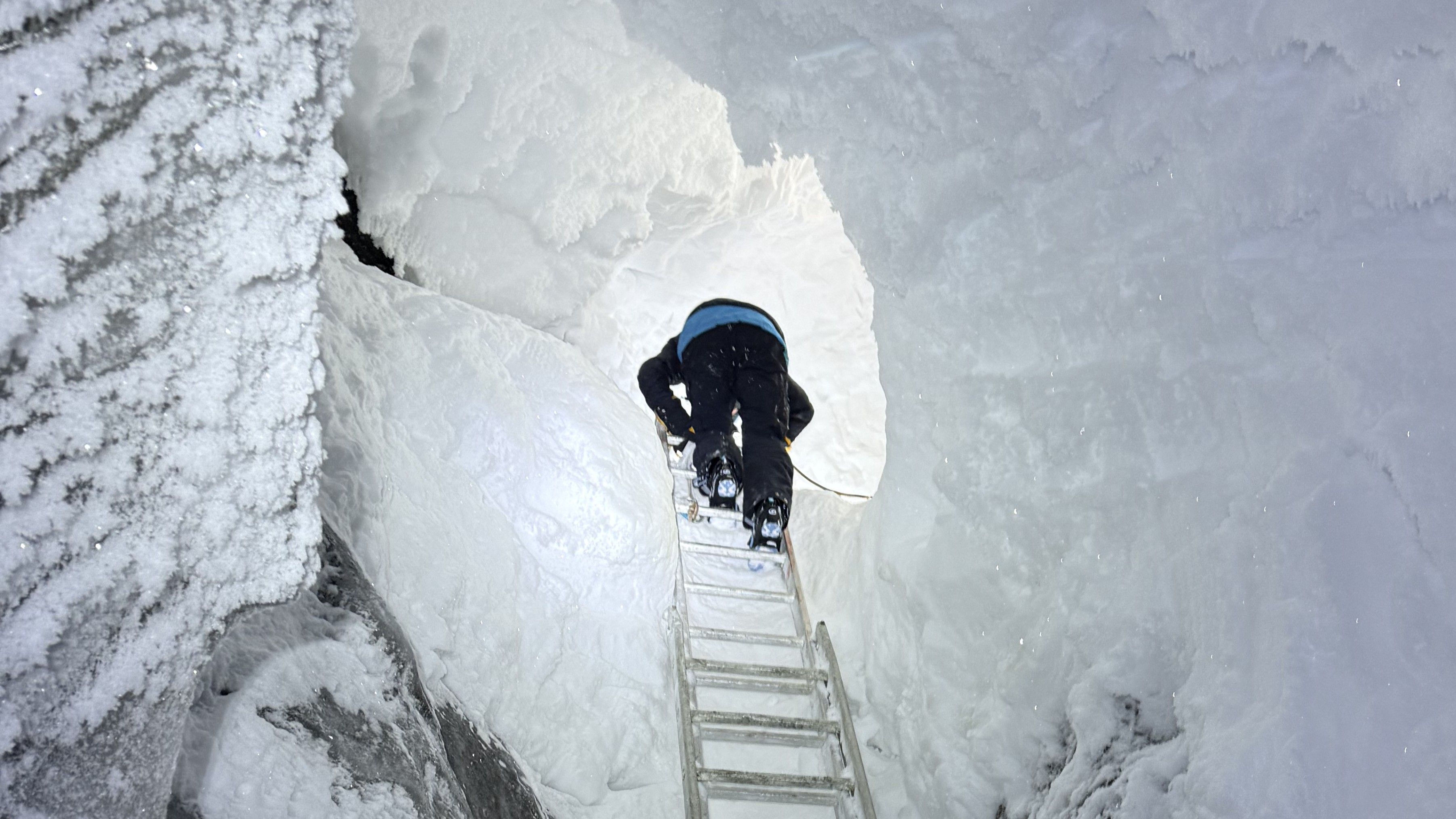 A person is climbing on a ladder at the entrence of the ice cave.