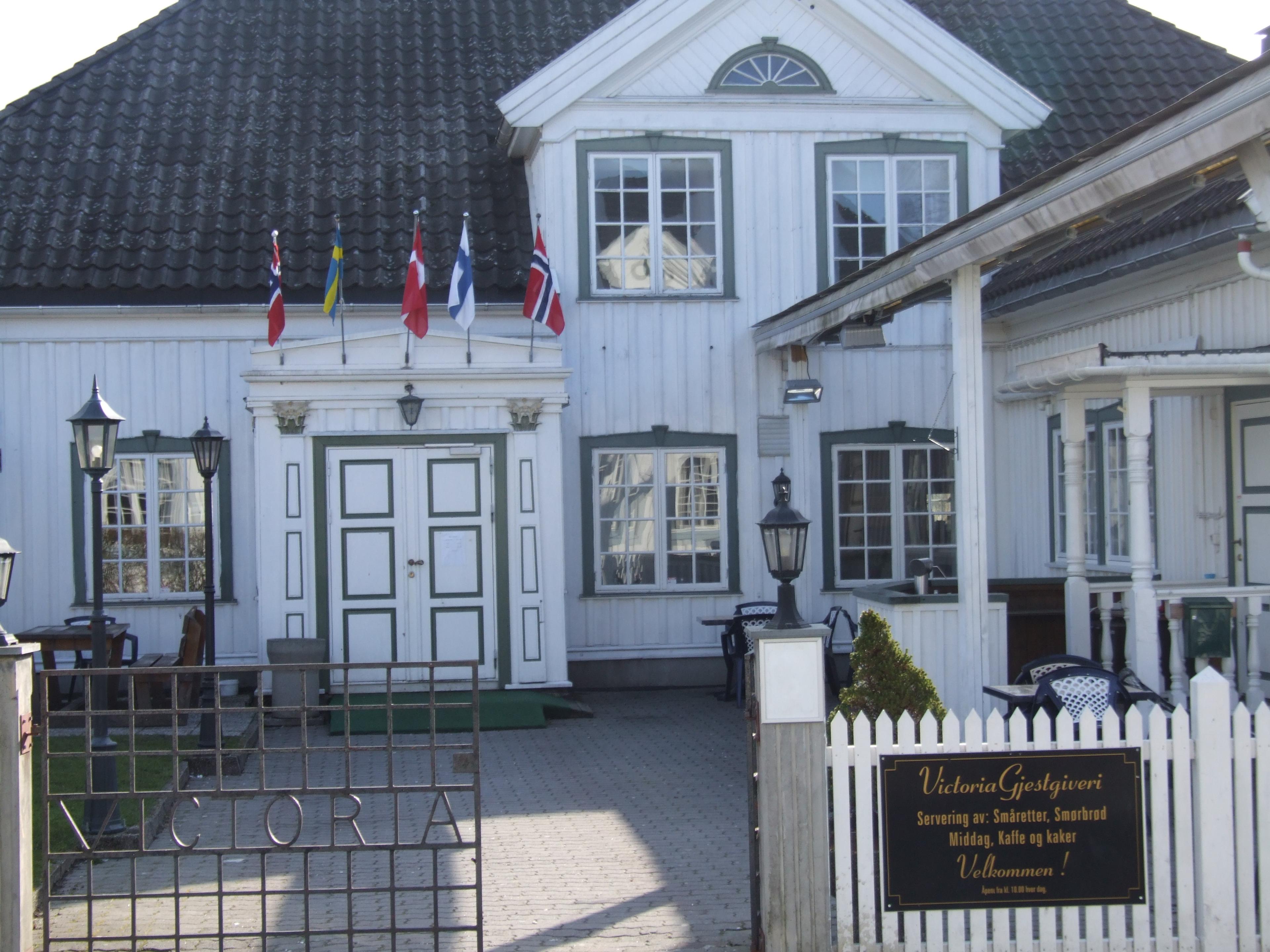 gammel hvit trebygning med blå vinduskarmer, smijernsport og flagg