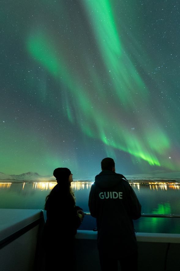 Two people viewing the Northern Lights from the boat's deck