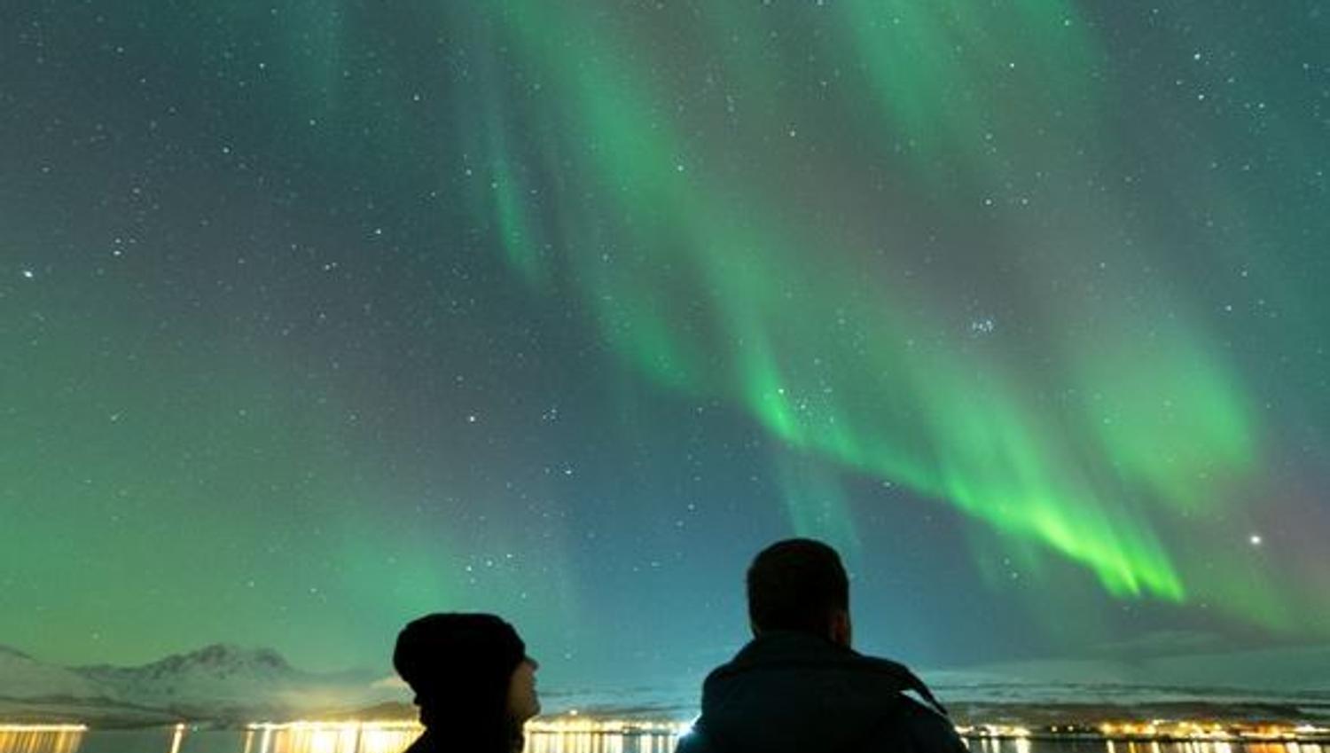 Two people viewing the Northern Lights from the boat's deck