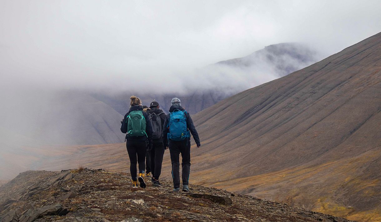 Three guests hiking on top of a hill with mist and mountains in the background