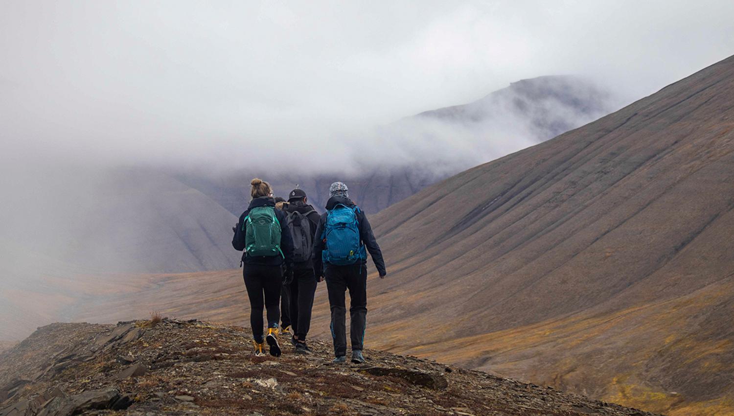Three guests hiking on top of a hill with mist and mountains in the background