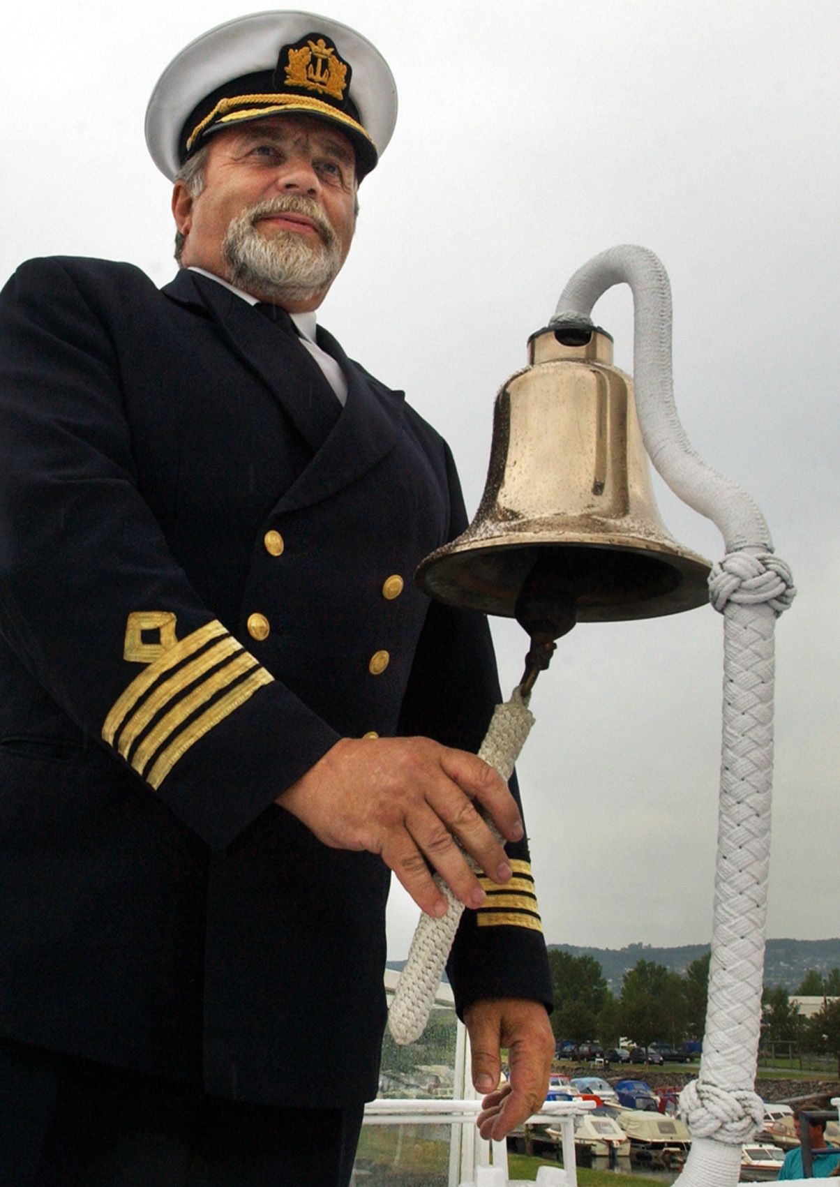 Båt kaptein i full uniform som ringer med den gamle skipsklokken på  Skibladner