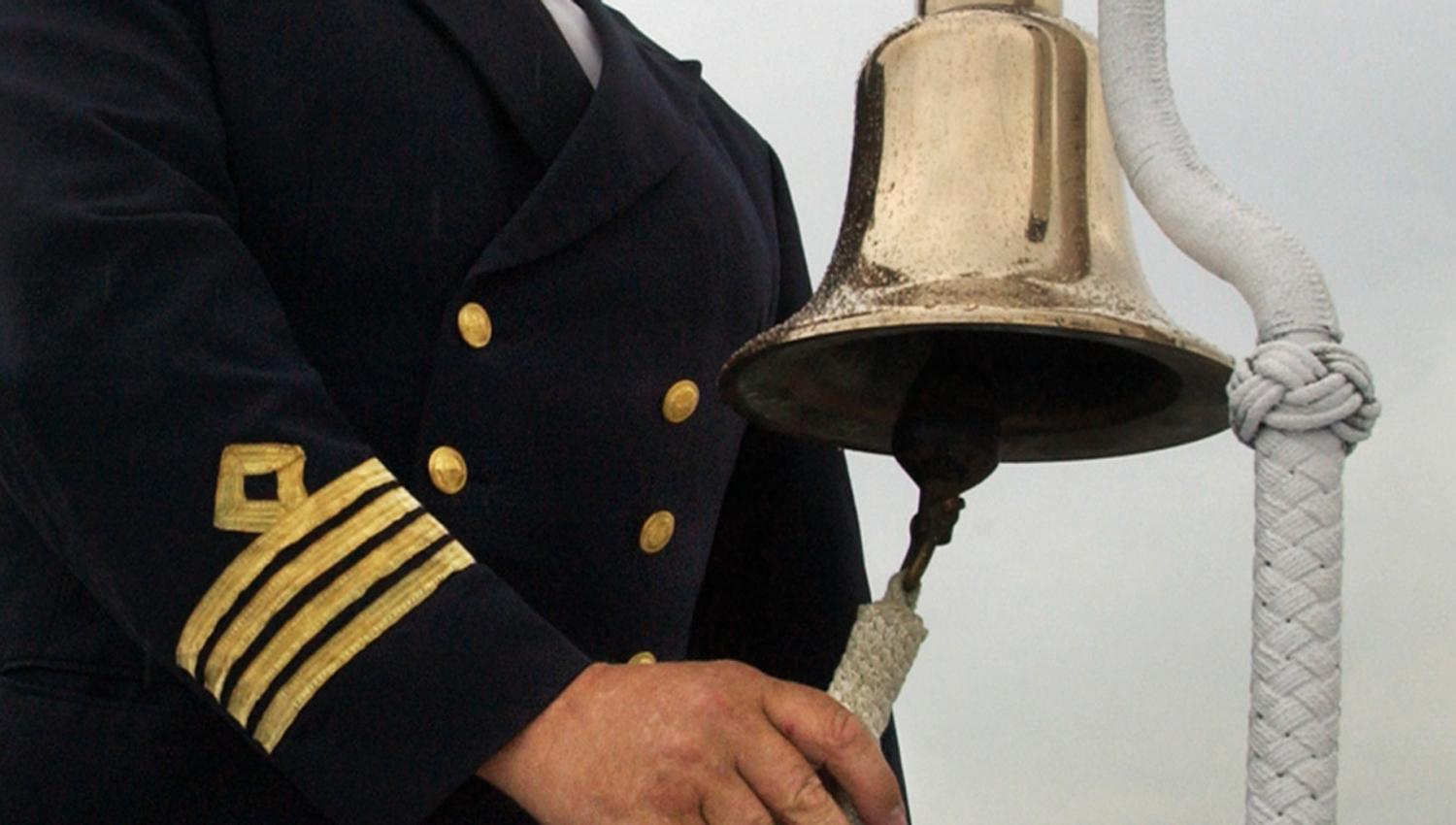 Båt kaptein i full uniform som ringer med den gamle skipsklokken på Skibladner