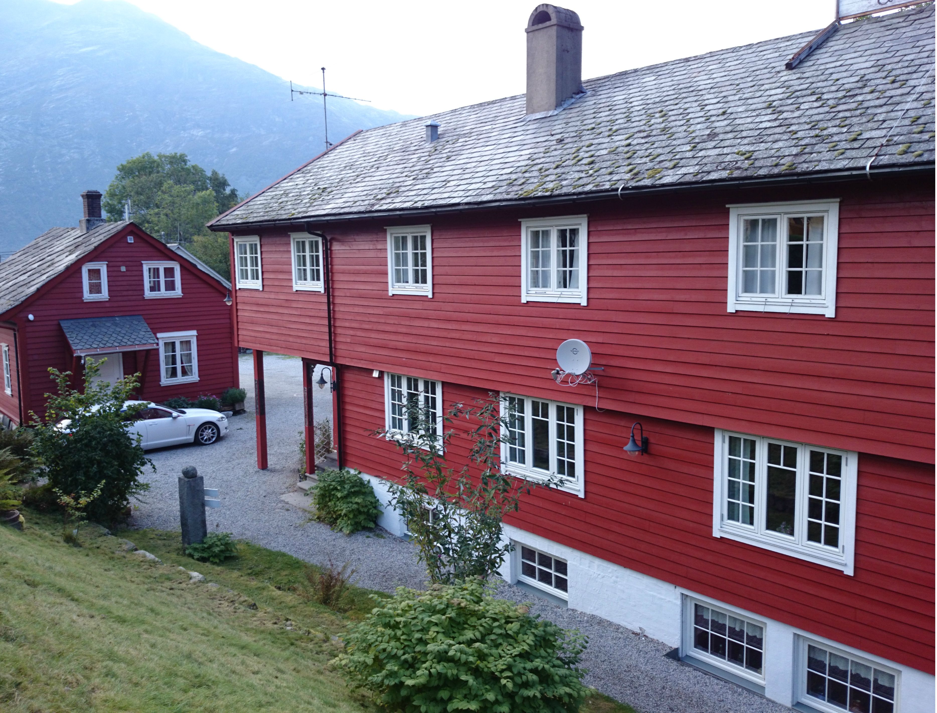 Raudmåla hovudbygg og tun på Ullensvang Gjesteheim, omkransa av fjell, frukthagar og tradisjonell vestlandsidyll.