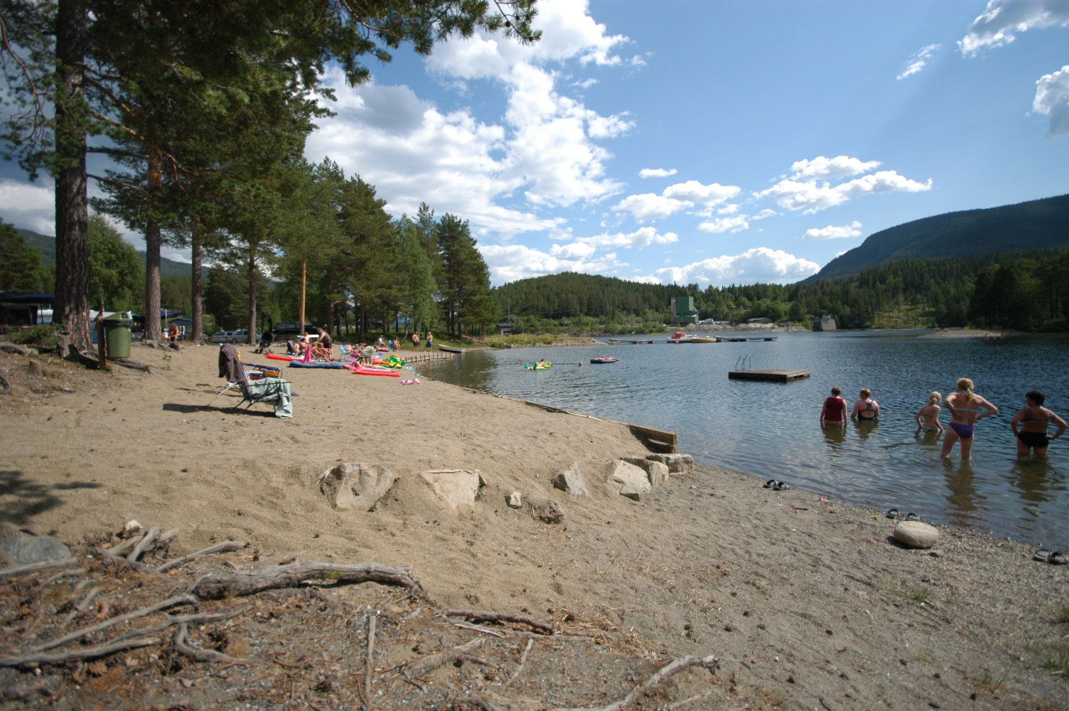 A sandy beach by a lake with people enjoying a swim and the sun.