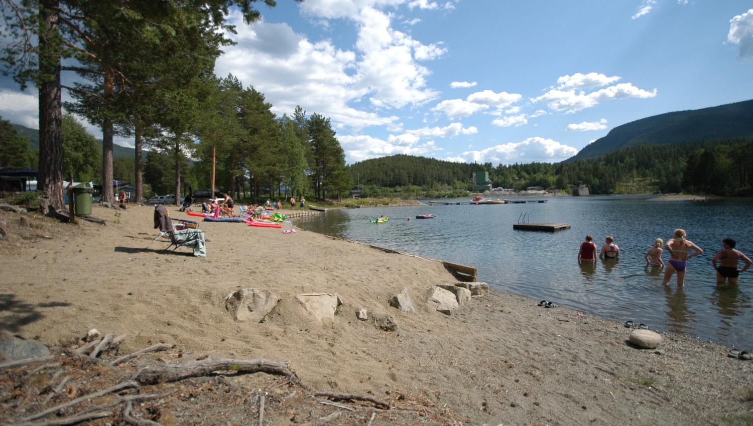 A sandy beach by a lake with people enjoying a swim and the sun.