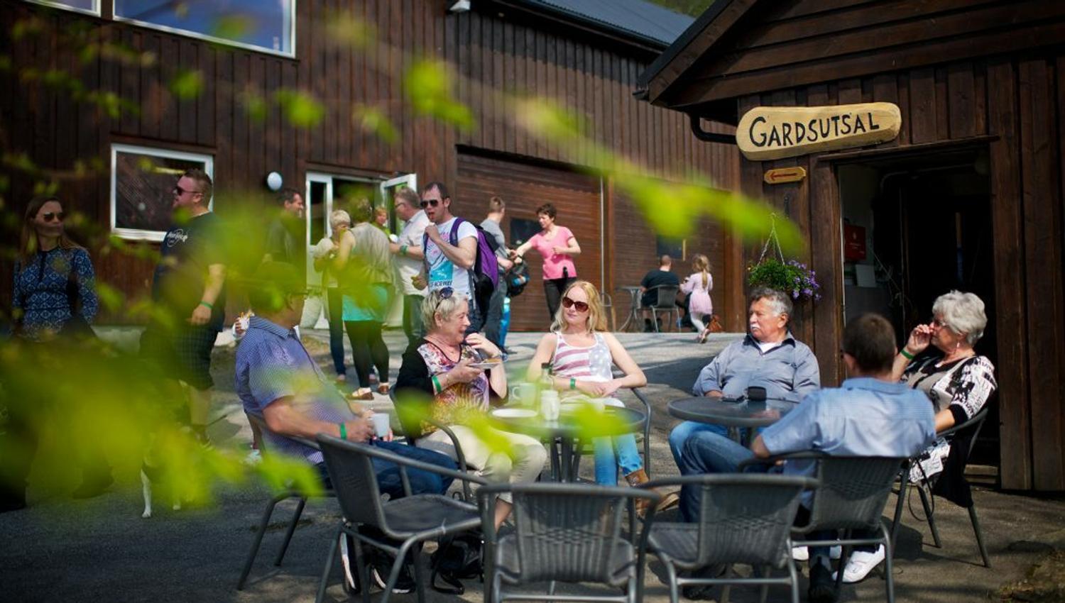 Gruppe sit ute ved Gardsutsalet i Ulvik på ein solrik dag.