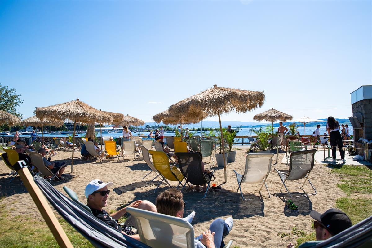 Strandområde med solsenger, parasoller og mennesker som slapper av i solen.