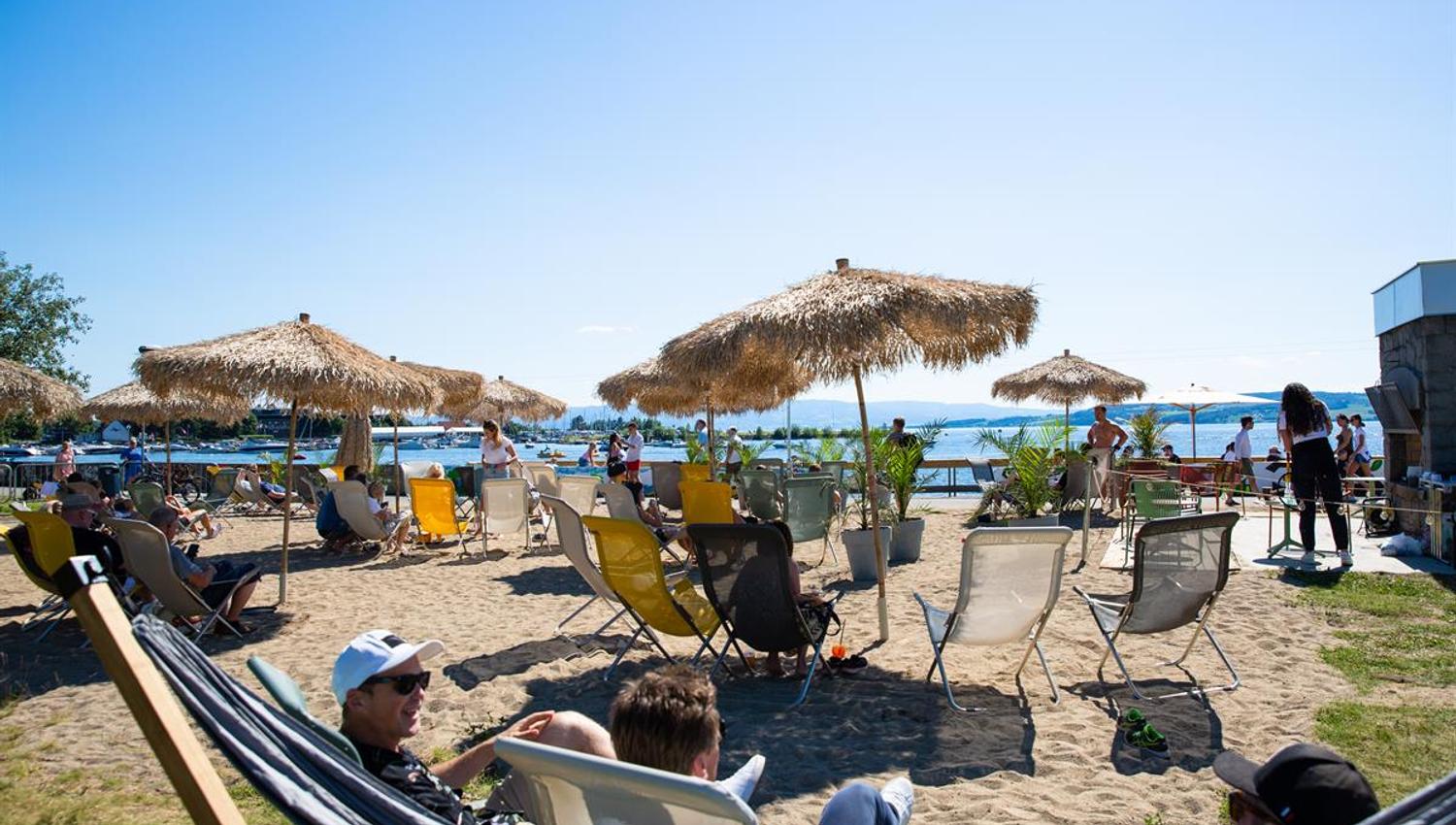 Strandområde med solsenger, parasoller og mennesker som slapper av i solen.