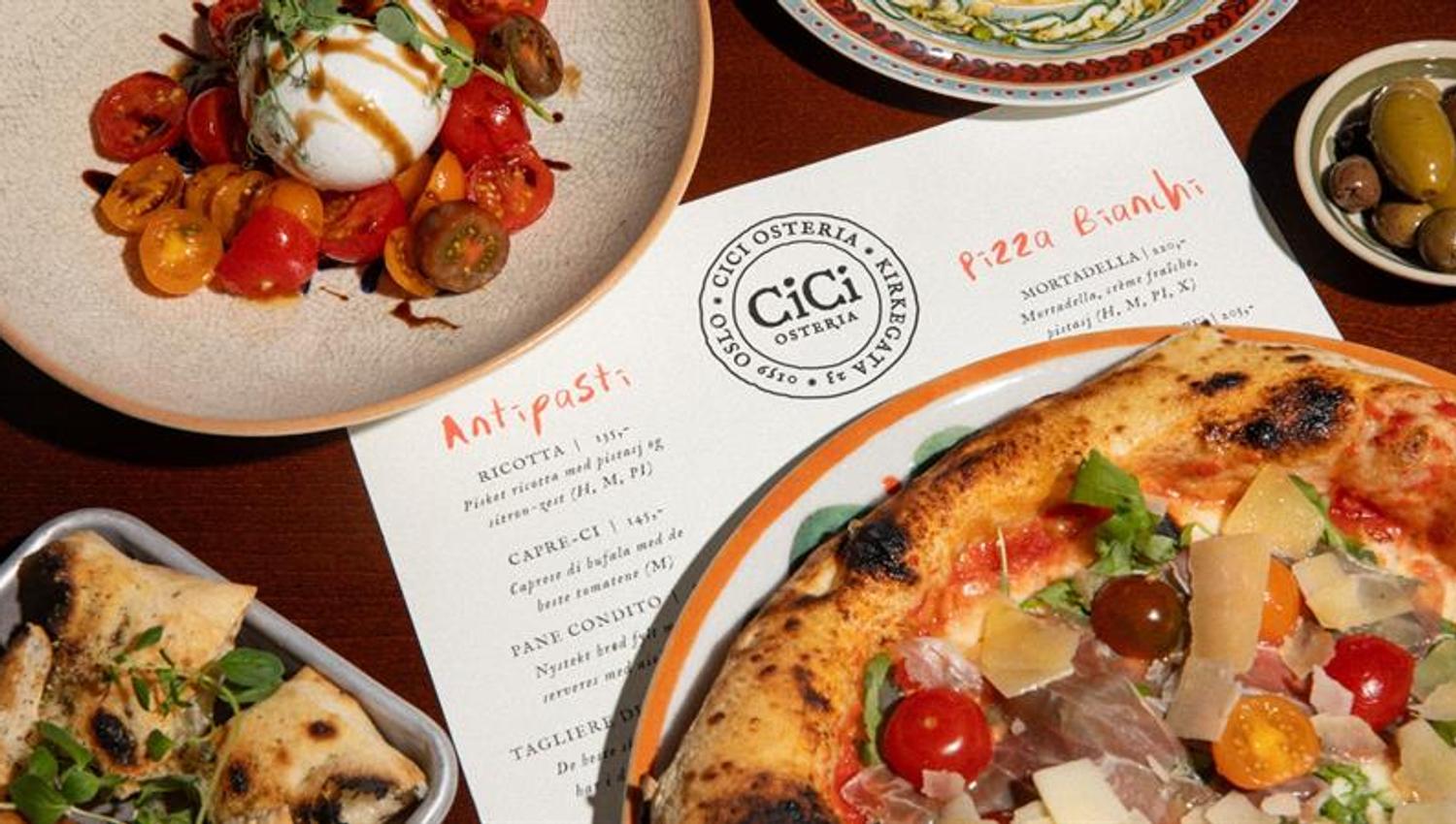 Close-up of a pizza and various side dishes on a dining table next to a menu and cutlery