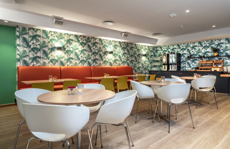 Round wooden tables, white chairs, red seating area, colorful wallpaper on the walls.