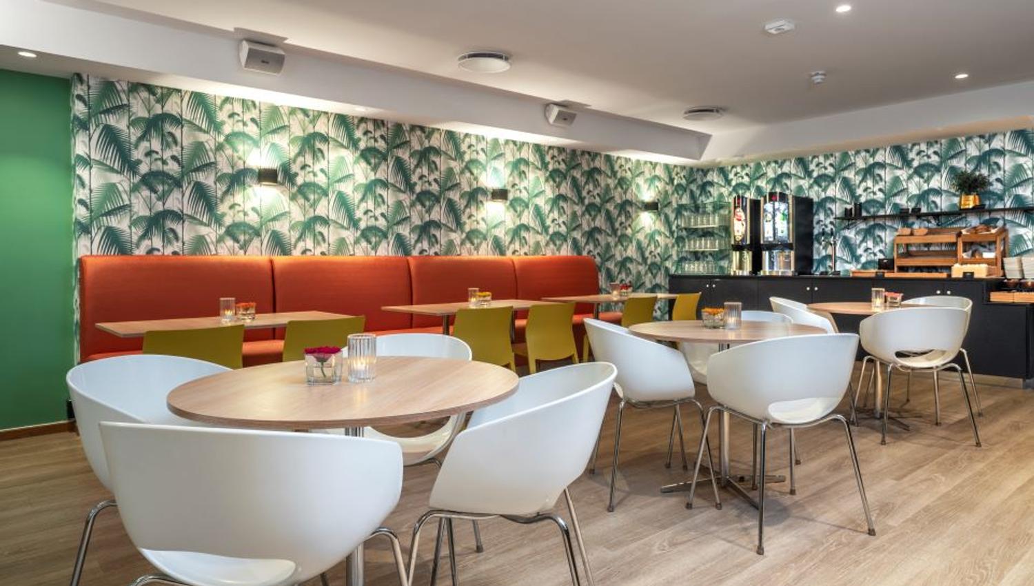 Round wooden tables, white chairs, red seating area, colorful wallpaper on the walls.