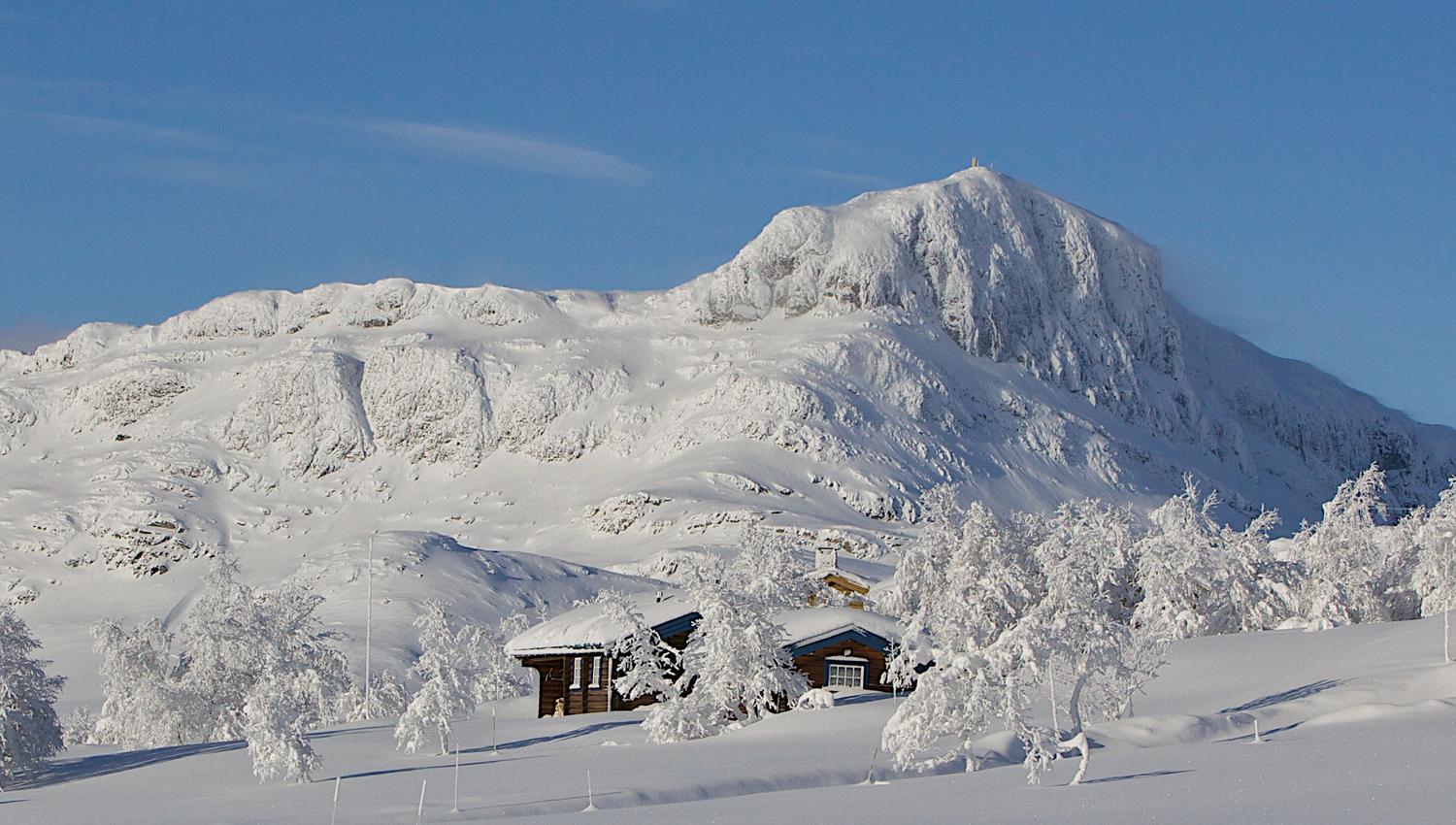 Hytte med det vinterkledde fjellet Bitihorn i bakgrunnen.