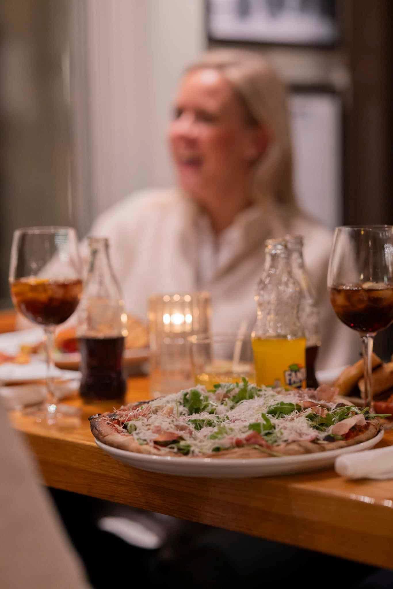 Pizza fra SMOI i fokus og i bakgrunnen kan man se en smilende gjest