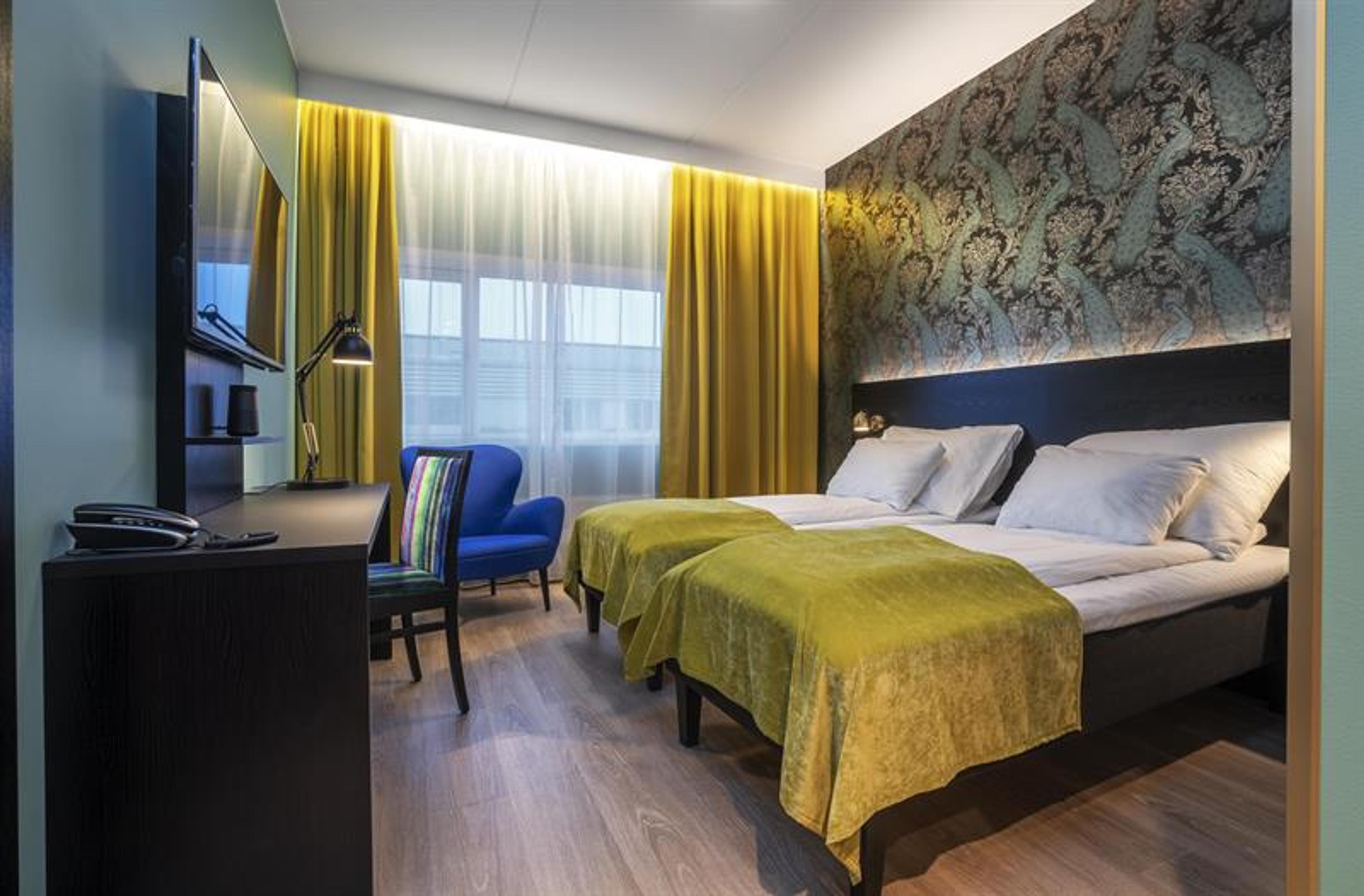 hotell rom med ddobbeltseng med gult sengeteppe og en blå stol